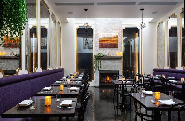 This is a photo of a dining room at Ivy Lane, with a purple banquette and gray brick fireplace.
